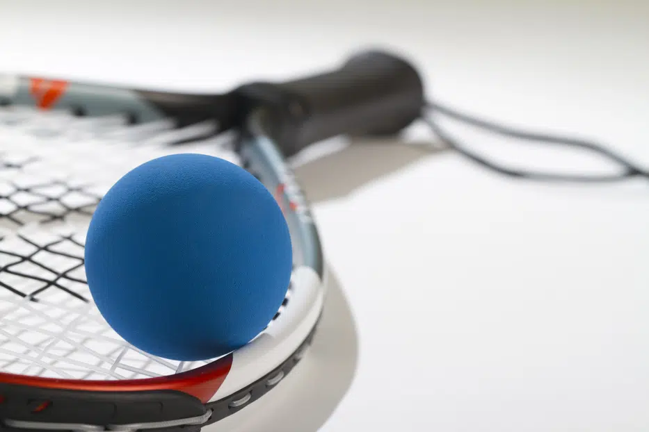 blue racquetball in foreground laying on racquet strings. Handle is blurred.